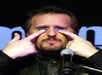 A man holding quarters over his eyes in front of a microphone on stage at The Mentalist in Las Vegas.