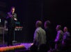 A man in all black on stage holding a microphone interacting with guest who are standing in front of the stage at The Mentalist in Las Vegas.