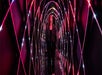 A woman in a black jacket walking through a dark tunnel with criss cross magenta lights on the walls going over her head.