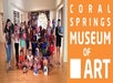 A group of children posed together holding up masks they have made at the Coral Springs Museum of Art.