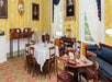 A dining room with a round table set for a meal, antique wooden chairs, a blue sofa, and portrait paintings on yellow patterned walls.