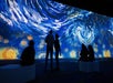 Four people sit and stand in front of a large digital projection of Van Gogh's "The Starry Night" in a dark exhibition space.