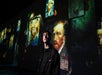 A person stands in front of a wall displaying multiple projected images of Vincent van Gogh’s self-portraits and paintings.