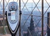 Coin-operated binoculars on an observation deck with a view of a city and a distinctive skyscraper in the background.