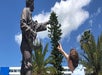 A man reaching up to touch a statue that has its hand out with a blue sky behind them on the Scavenger Hunts - Orlando.