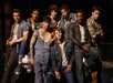 A group of eight people, dressed in casual and denim clothing, pose together in front of a car.