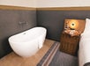 A floor-mounted free standing white oval tub with a night stand with snacks and wine on it and white bed next to it in a hotel room.