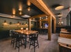 A dining area with rustic rectangle tables and black chairs with small lamps on the left, and square tables with brown chairs on the right.