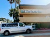 A white van with "The Pacific Inn" logo is parked in front of The Pacific Inn hotel building on a sunny day, with palm trees in the background.