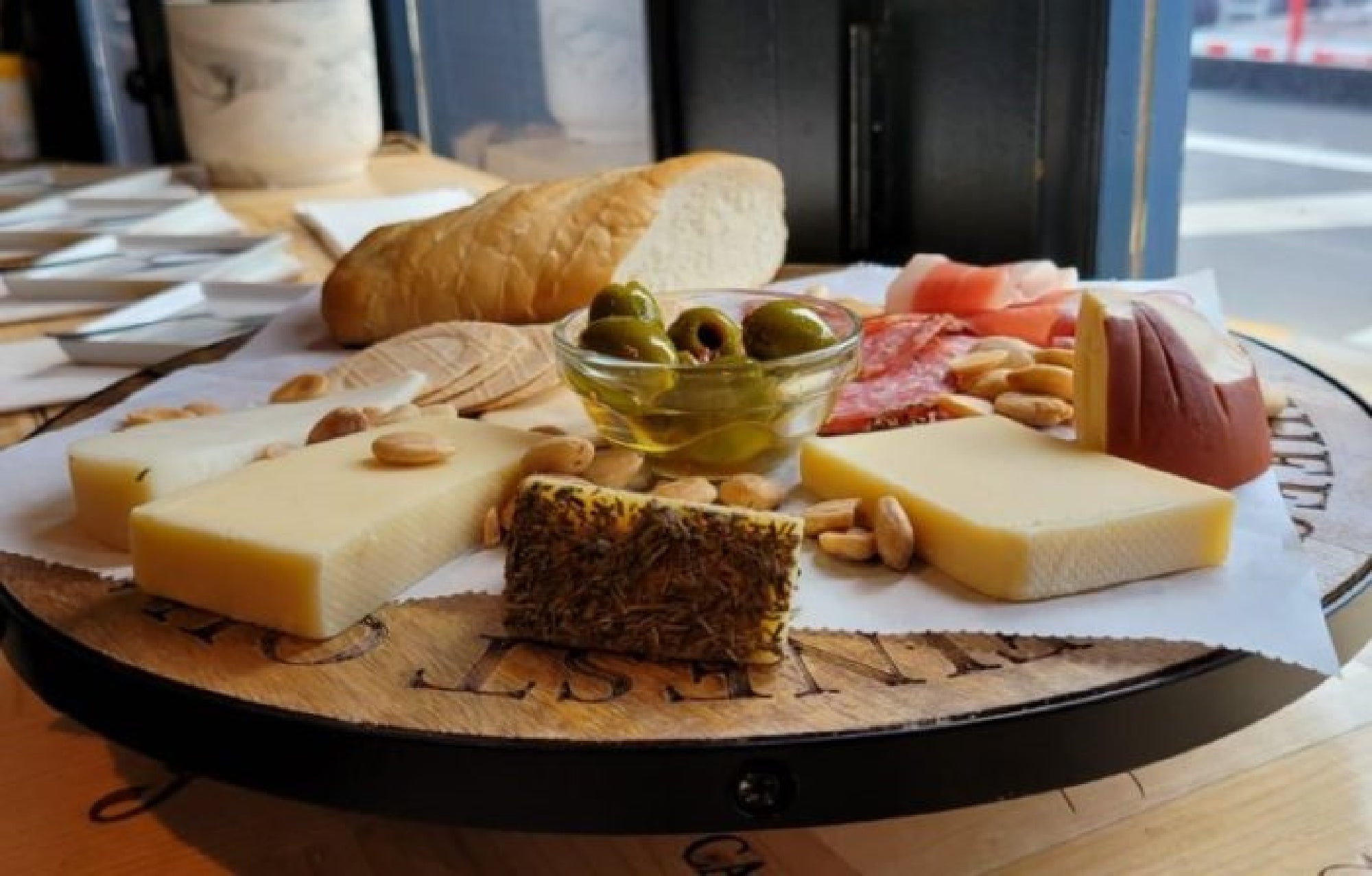 A charcuterie board with various cheeses, a bowl of olives, sliced bread, nuts, and cured meats arranged on a round tray.