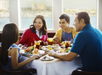 A family of four sits at a table with seafood dishes and drinks, smiling and talking, by a window overlooking water.
