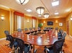 A large conference room with a U-shaped table arrangement, ergonomic chairs, water glasses, and decorative lighting. Walls are warm-toned with framed artwork and a mounted television.