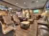 Upscale lounge with leather seating, patterned armchairs, wooden tables, and multiple wall-mounted TVs, one displaying a sports game.