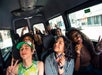 A group of people sitting inside a van smile and pose for the camera, some holding snacks and making peace signs.