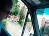 A person looks out a car window at a colorful mural painted on a wall in an urban area with buildings and trees in the background.