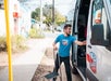 A man in a blue "Austin Detours" shirt pulls out a van step stool while standing next to an open van door on a sidewalk.