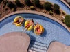 Three people relax on yellow inflatable rafts in a winding lazy river, surrounded by landscaped greenery.