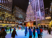 People ice skating at Rockefeller Center, New York, with a large, brightly lit Christmas tree and surrounding tall buildings.