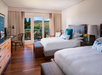 A hotel room with two double beds, wooden flooring, a balcony with a scenic view, and modern decor.