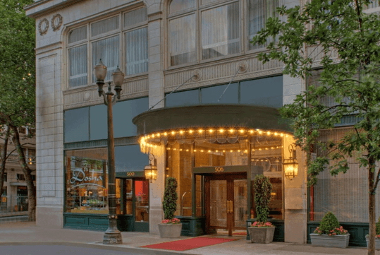The front entrance to the The Royal Sonesta Portland Downtown with warm lights hanging over it at dusk.