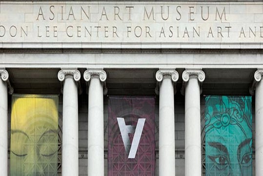 Facade of the Asian Art Museum with stone columns and large colorful banners displaying abstract designs and a prominent letter "A" in the center.