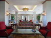Elegant lounge with red armchairs and patterned sofa around a glass coffee table. Soft lighting and decorative vases add to the classic ambiance. Large windows and dining area in the background.