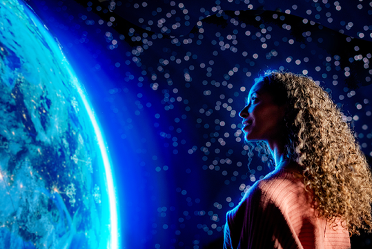 A woman with curly hair viewing Darren Aronofsky's inaugural multi-sensory film with blue light shining on her face.