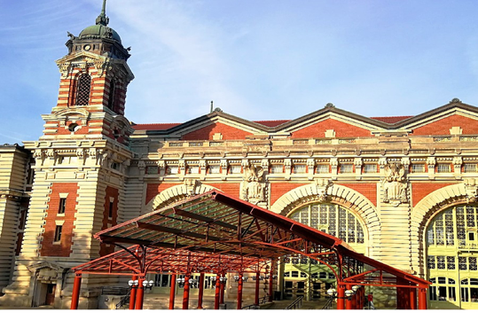 Ellis Island Immigration Museum with arched windows and a clock tower, under a blue sky.