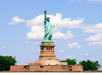 The Statue of Liberty stands on a pedestal with a backdrop of clouds and trees, as people gather at its base.