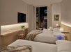 Modern hotel room with two neatly made beds, muted decor, a wall-mounted TV, and a window view of a cityscape. A small desk, chair, and flowers add to the ambiance.