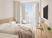 A minimalist hotel room with a king bed, soft bedding, a modern armchair, a wall-mounted TV, and a desk. Large windows with sheer curtains offer a cityscape view.