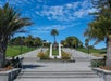 A broad concrete staircase leads to a large walkway lined with palm trees and a statue in the center. People are sitting and walking around the green areas on a clear, sunny day.