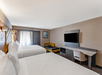 Two king beds, seating area, a desk and chair, and a wall-mounted TV inside a suite.