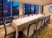 A long dining table set for a formal meal in a private room with a cityscape view through large windows.