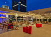 Outdoor rooftop space at night with string lights, patio seating, umbrellas, a giant Connect Four game, and large red buckets arranged for a game on the open patio.