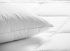 Close-up of a white pillow on a white quilted mattress surface.