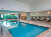 Indoor swimming pool area with lounge chairs, a small hot tub, and a view of the gym through glass walls.