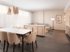 Modern dining and living area with beige chairs, white table, pendant light, and minimal decor.