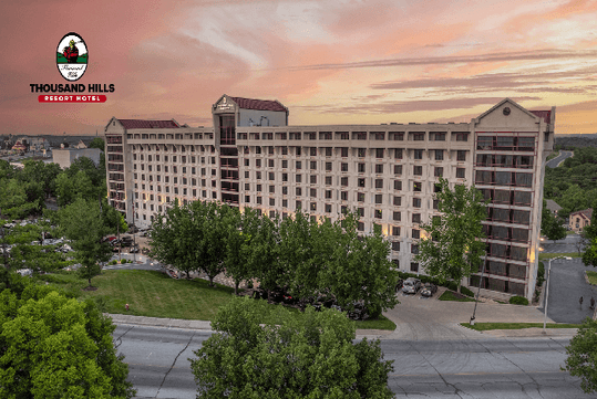 Aerial view of the exterior of the Thousand Hills Resort Hotel  with the sun setting in a cloudy sky behind it.