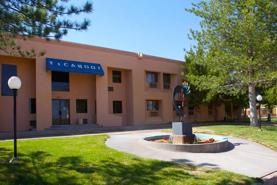 A building with a blue awning labeled "Ticaboo" and a metal sculpture in front, surrounded by grass and trees.