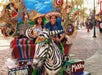 Two people wearing sombreros sit on a donkey painted like a zebra, surrounded by colorful decorations and signs reading "Tijuana" and "Mexico" on a street.