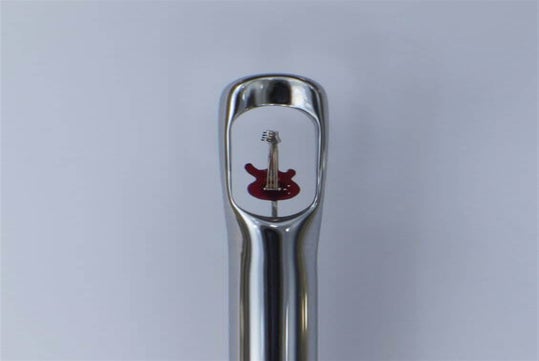 A miniature red guitar is positioned inside the eye of a large sewing needle against a plain background.