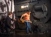 A boy shovels coal into a large furnace replica while a man dressed as a train engineer kneels nearby, supervising the activity.