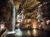 Visitors ride a golf cart through the Lost Canyon cavern with waterfalls cascading nearby.