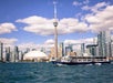 A boat travels across the water in front of the Toronto skyline, with the CN Tower and Rogers Centre visible under a partly cloudy sky.