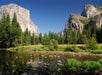 Wide shot of Yosemite National park from Merced River on a bright sunny day with a clear blue sky.