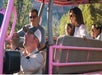 Four people sit in the back of an open-air pink jeep while a driver in a cap navigates. Trees and rocky terrain are visible in the background.