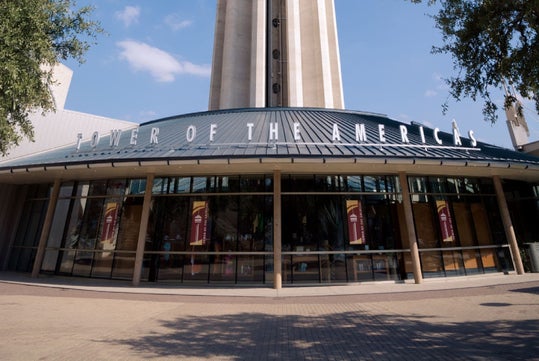 The entrance to the Tower of the Americas in San Antonio, with the building's name displayed above glass doors and windows.