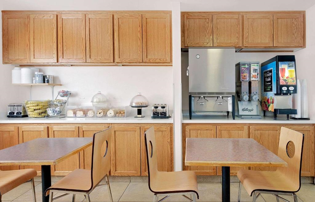 Breakfast area with wooden tables and chairs. Cabinets above and below offer storage. Counter features cereal dispensers, a juice machine, and pastries in glass domes.