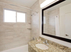 Modern bathroom with beige tiled walls, a bathtub-shower combo, granite countertop with sink, large mirror, and a frosted window.